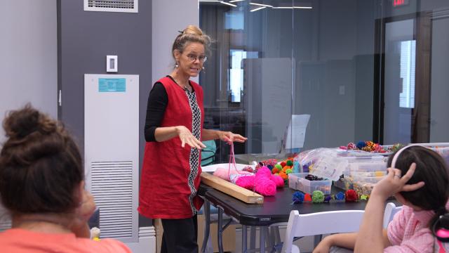 Dawne Hoeg stands at a table with yarn speaking to a group of students