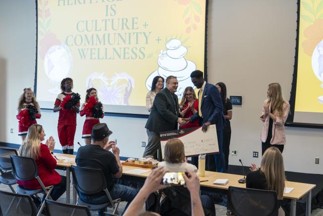 people stand on stage, one hands a oversized check to the student who won.