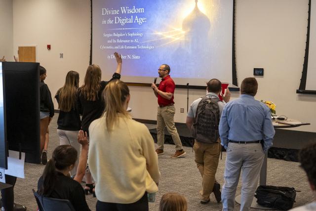 person standing at the front of a room with a microphone and audience is raising hands asking questions