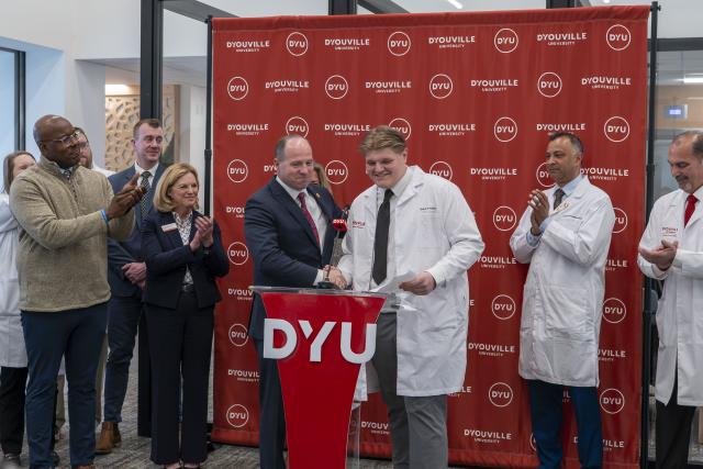 crowd claps while tim kennedy shakes the hand of a student in a white coat