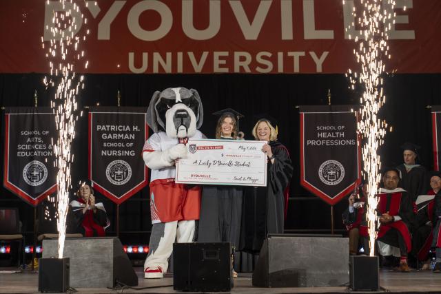 Saint the mascot stands with student and Dr. Lorrie Clemo with a giant check reading "Dog ate my debt"