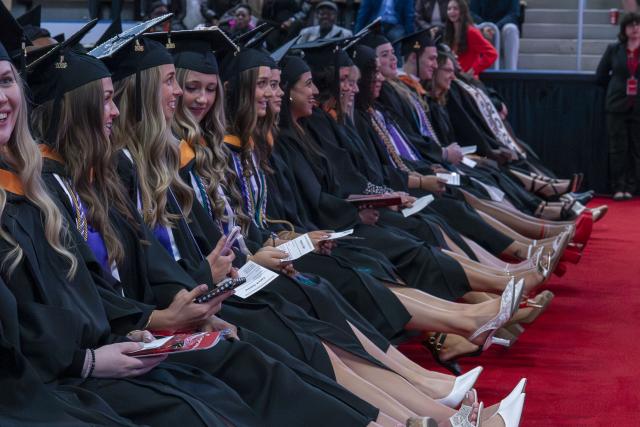 row of graduates in cap and gown regalia clapping their heels together