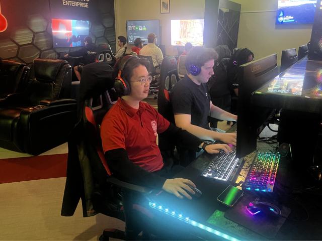 student sits at gaming desktop with other students 