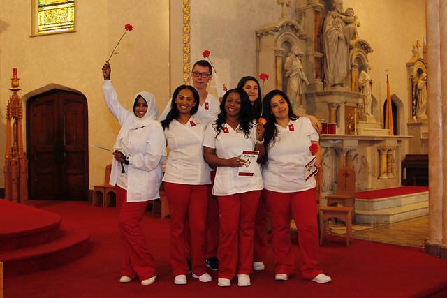 Five women and one man, dressed in matching red and white scrubs, pose with long stem roses in a church
