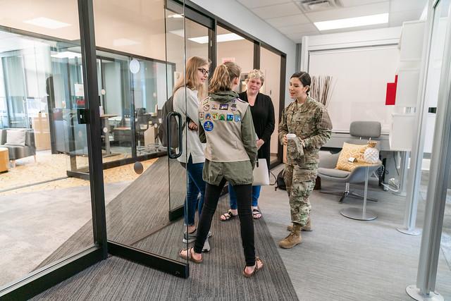 A woman dressed in camo talks with three women in a sitting room with glass walls
