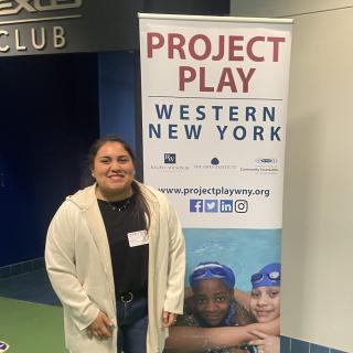Ellen Newton standing in front of a Project Play Poster
