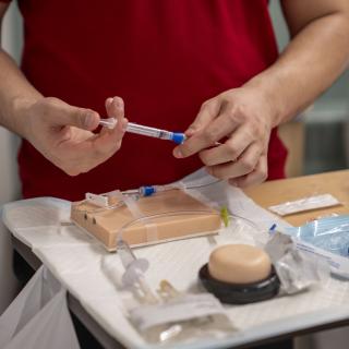 Nursing student practicing injections. Student pushes the plunger on a syringe connected to an IV.