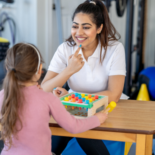 Young woman points to the shape of her mouth while a young child watches