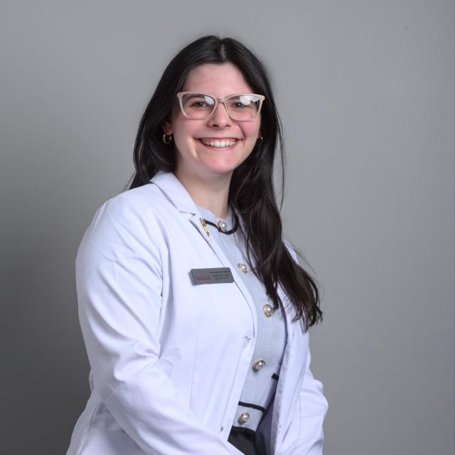 Woman smiles at the camera wearing a white coat