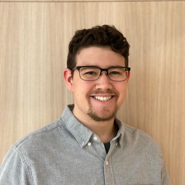 Man with dark hair and glasses smiles at the camera