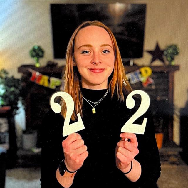Riley, Woman with blond hair smiles at the camera holding "22" sign.